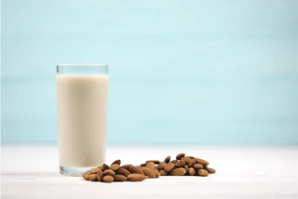 a tall glass of creamy almond milk next to a handful of raw almonds, on a clean kitchen counter or rustic wooden table.