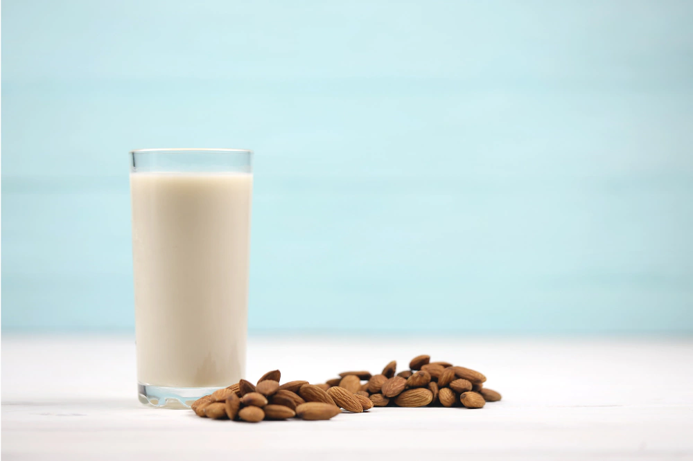 a tall glass of creamy almond milk next to a handful of raw almonds, on a clean kitchen counter or rustic wooden table.