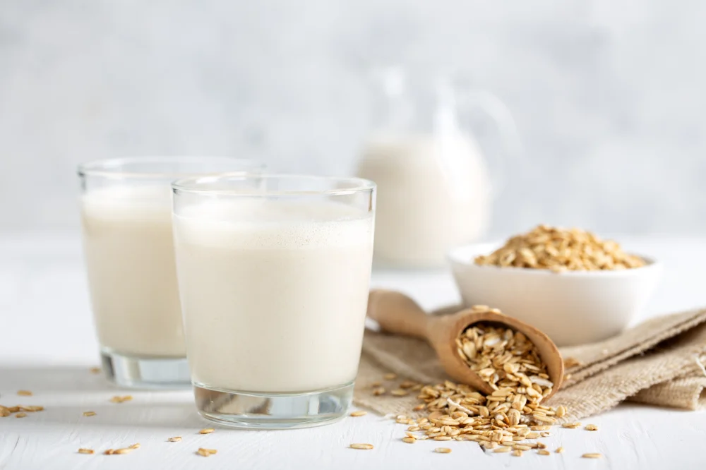 Un grand verre de lait d'avoine onctueux à côté d'un bol de flocons d'avoine.